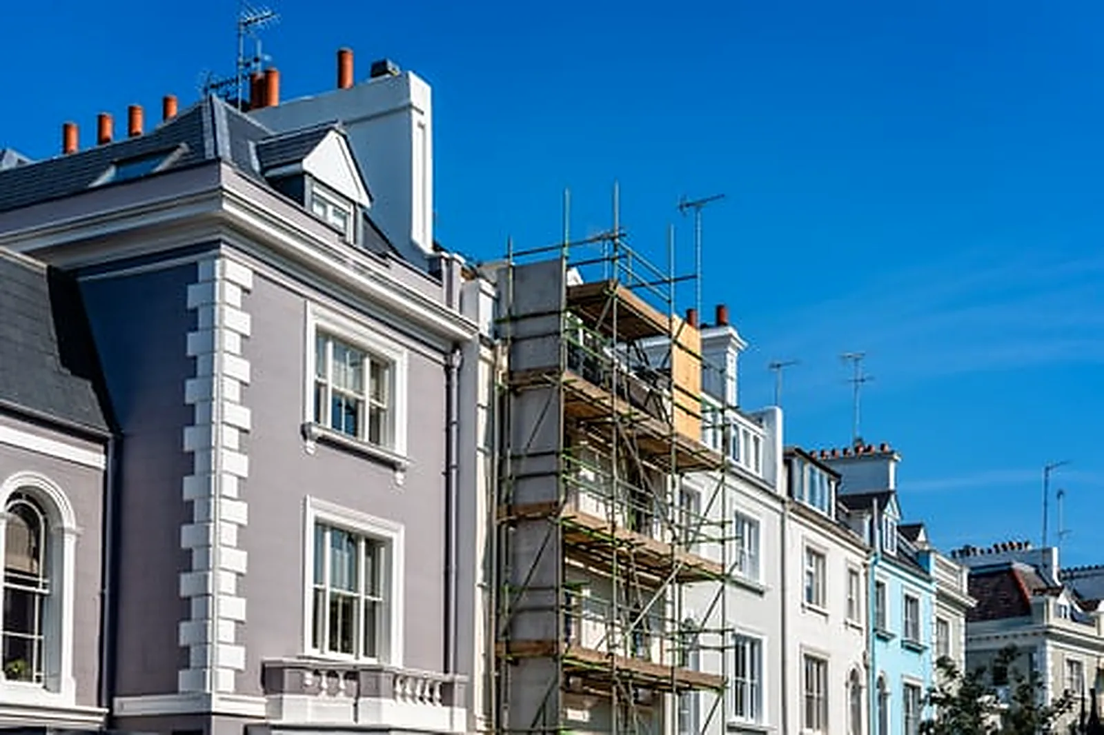 Scaffolding on a home facade during an exterior repaint job under a clear blue sky