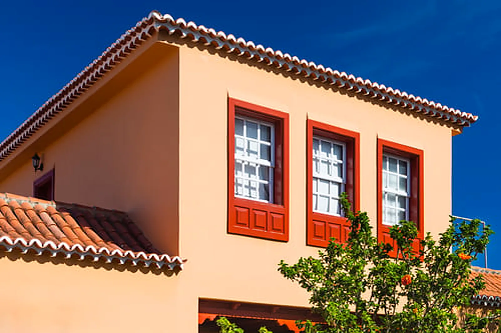 Sunlit two-story stucco home with freshly painted exterior walls and crisp red window trim