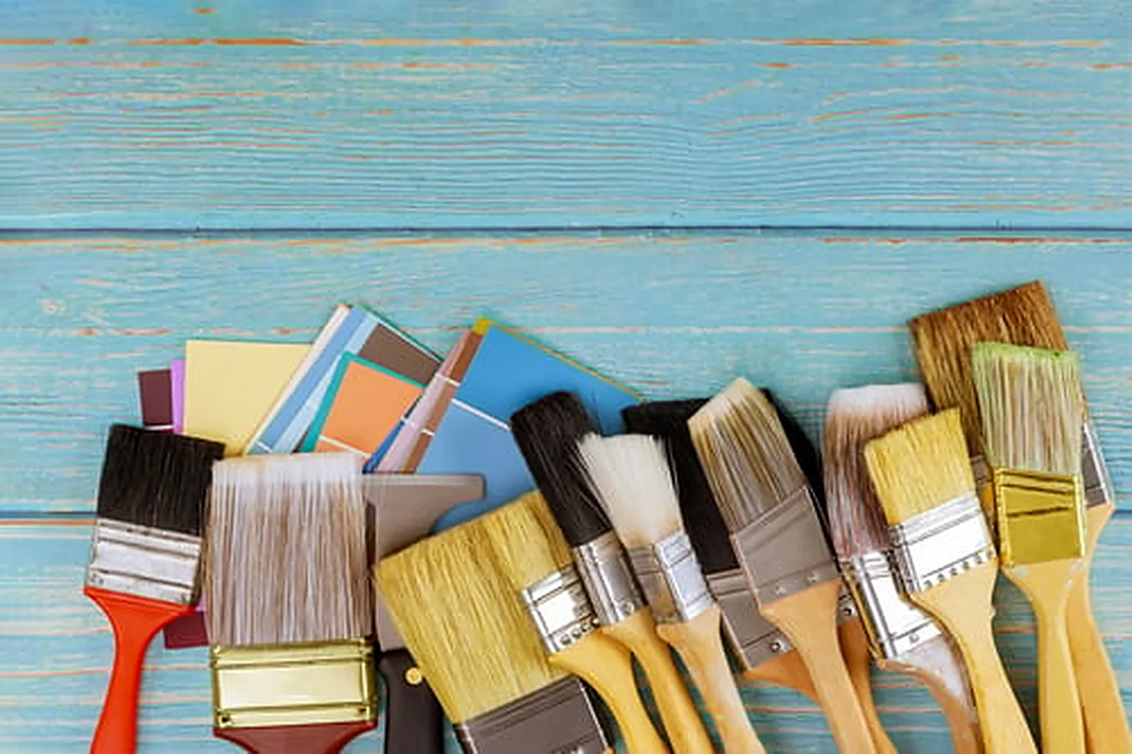 Row of well-used professional paint brushes and color swatches on a weathered turquoise wood workbench
