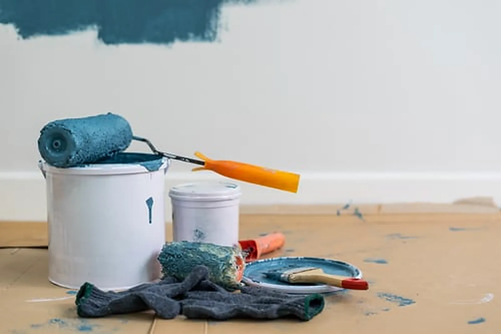 Interior wall being repainted in deep blue with a roller, paint bucket and covered floor in a bright room