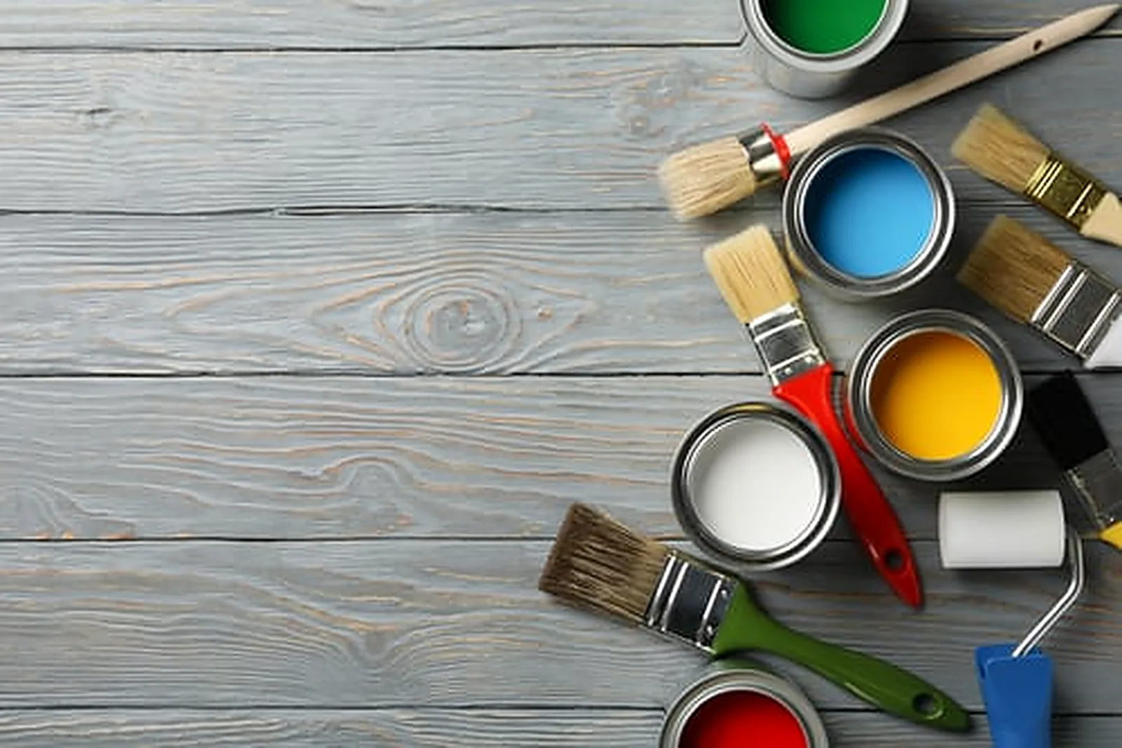 Professional painting tools, brushes and open cans of paint arranged on a weathered grey wood surface